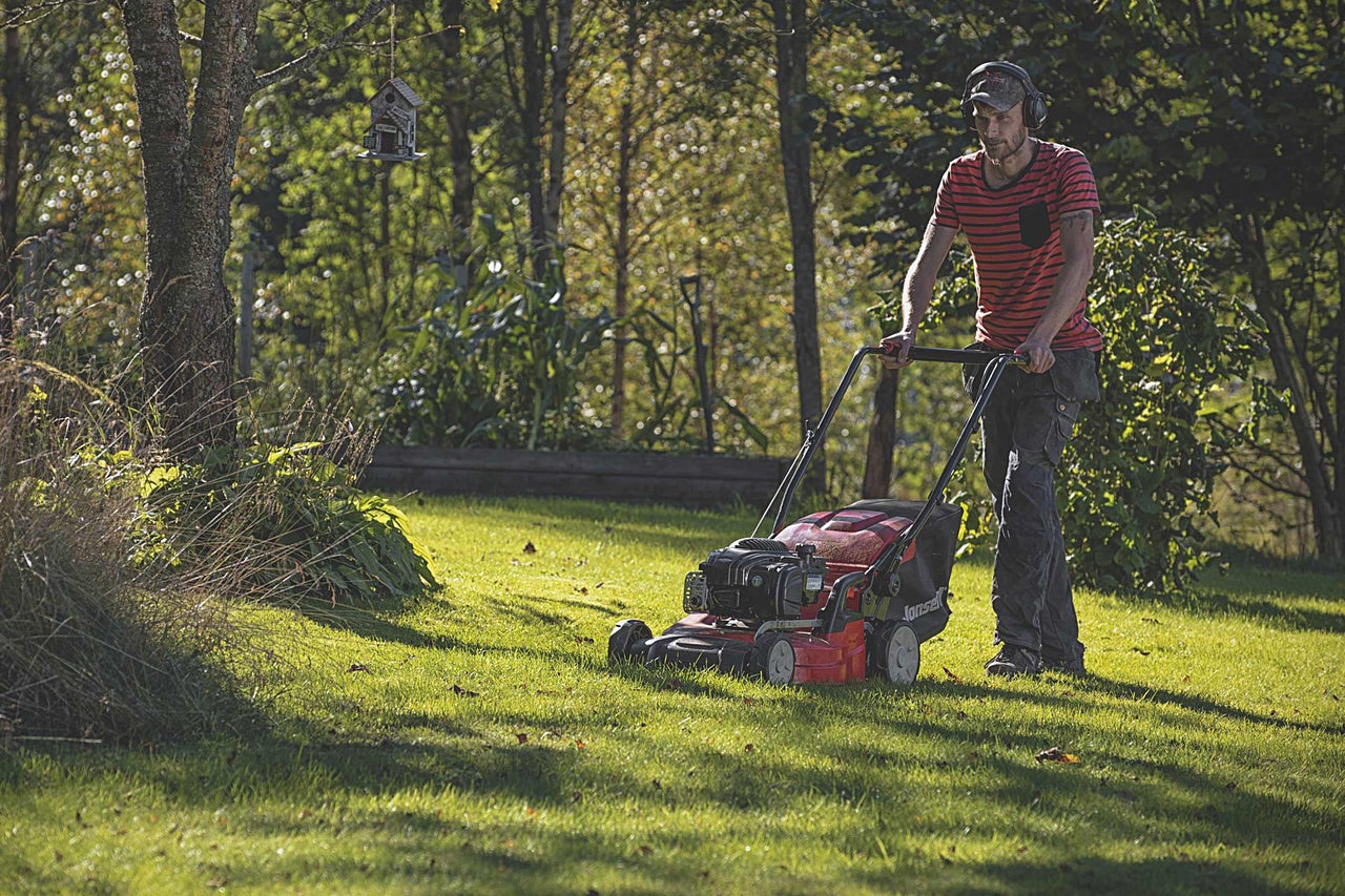 Un homme tond la pelouse avec une tondeuse à gazon dans le jardin.