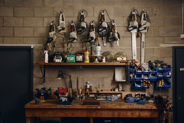 Atelier avec établi, étagères et divers outils tels que des tronçonneuses, une meuleuse et un étau.