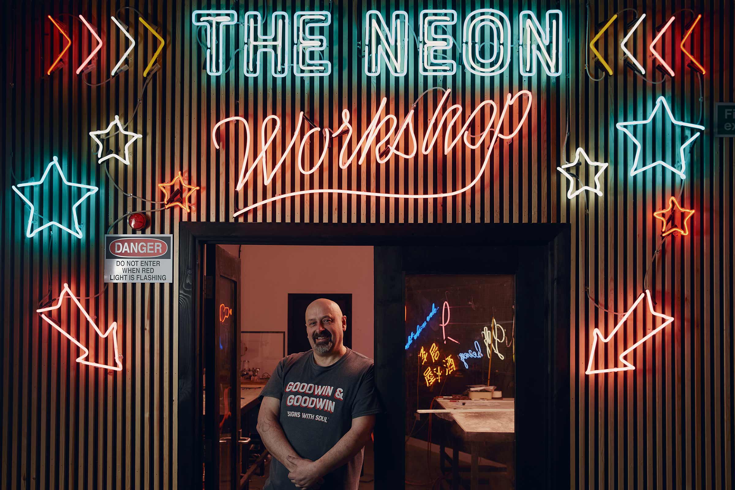 Entrée du Neon Workshop avec des enseignes au néon et un panneau d'avertissement