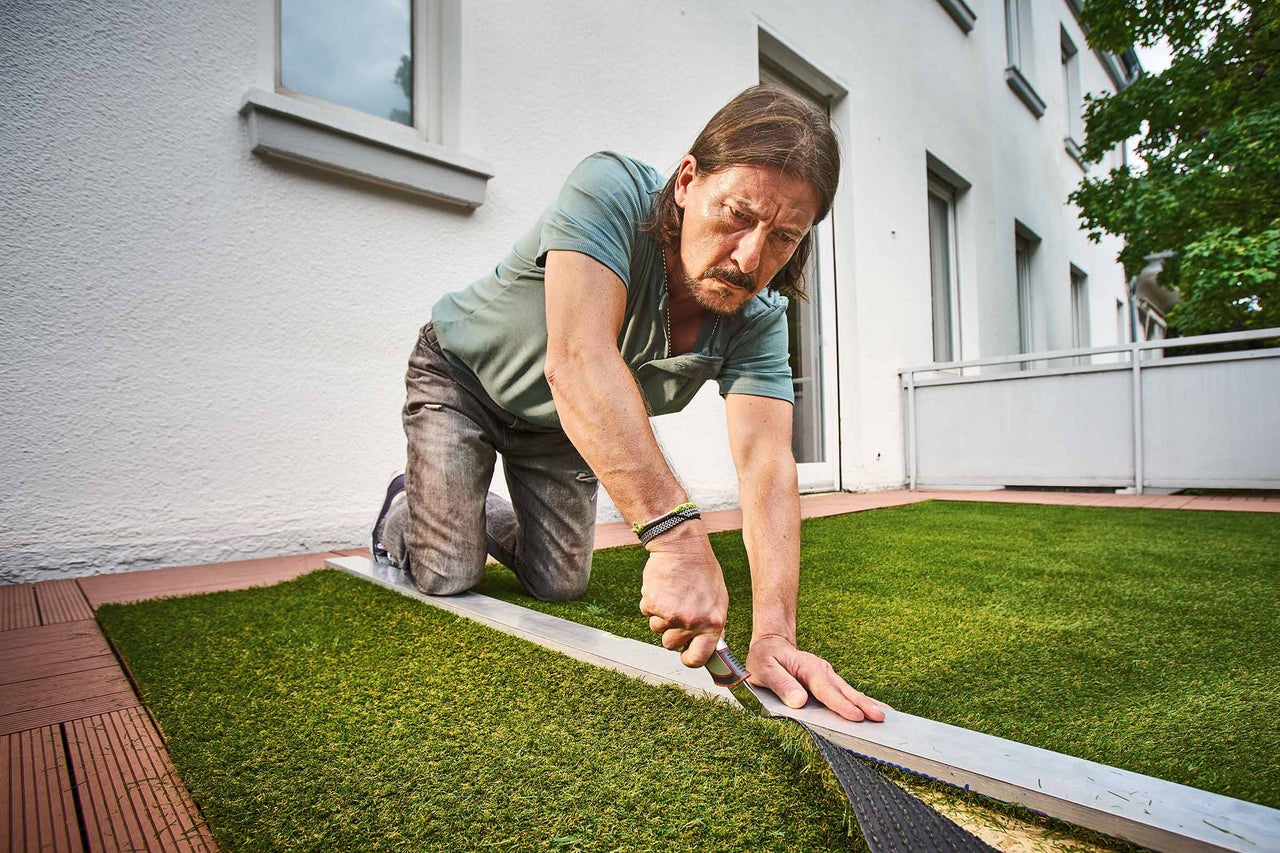 Un homme pose du gazon artificiel sur un balcon
