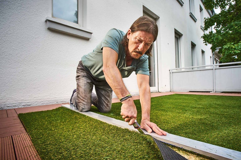 Un homme pose du gazon artificiel sur un balcon