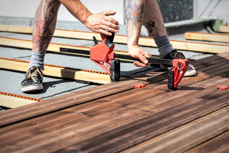 Mann verlegt eine Holzterrasse mit einer Schraubzwinge
