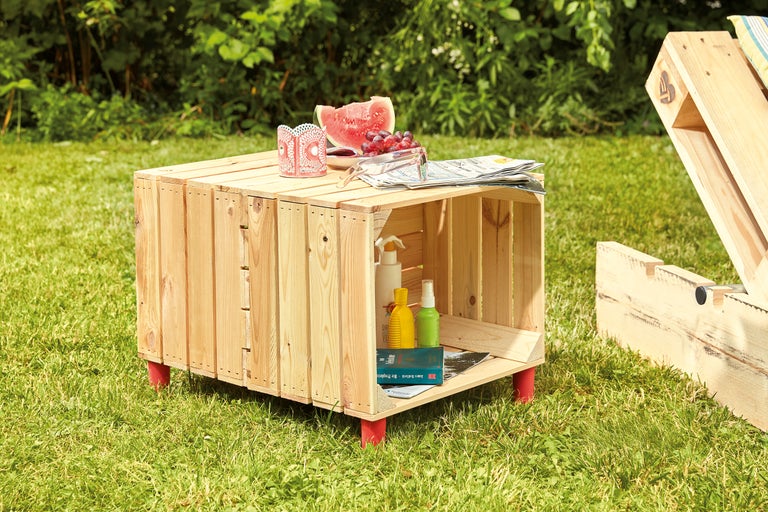 Gartenszene mit einem Holzkisten-Couchtisch, Getränken und Snacks auf einer Rasenfläche