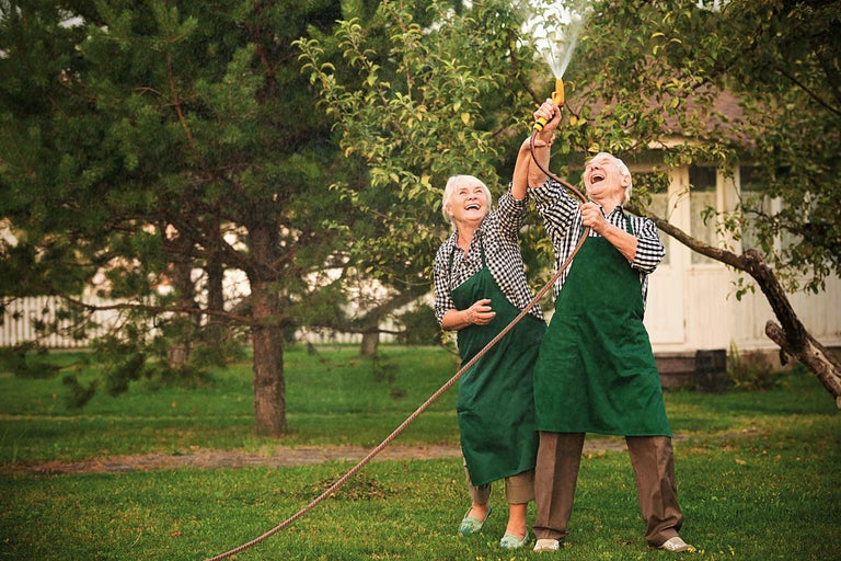 Couple âgé avec un tuyau d'arrosage dans le jardin