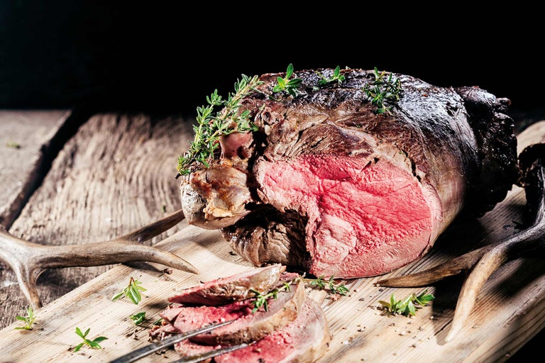Hirschbraten mit Kräutern auf einem Holzbrett, teilweise angeschnitten