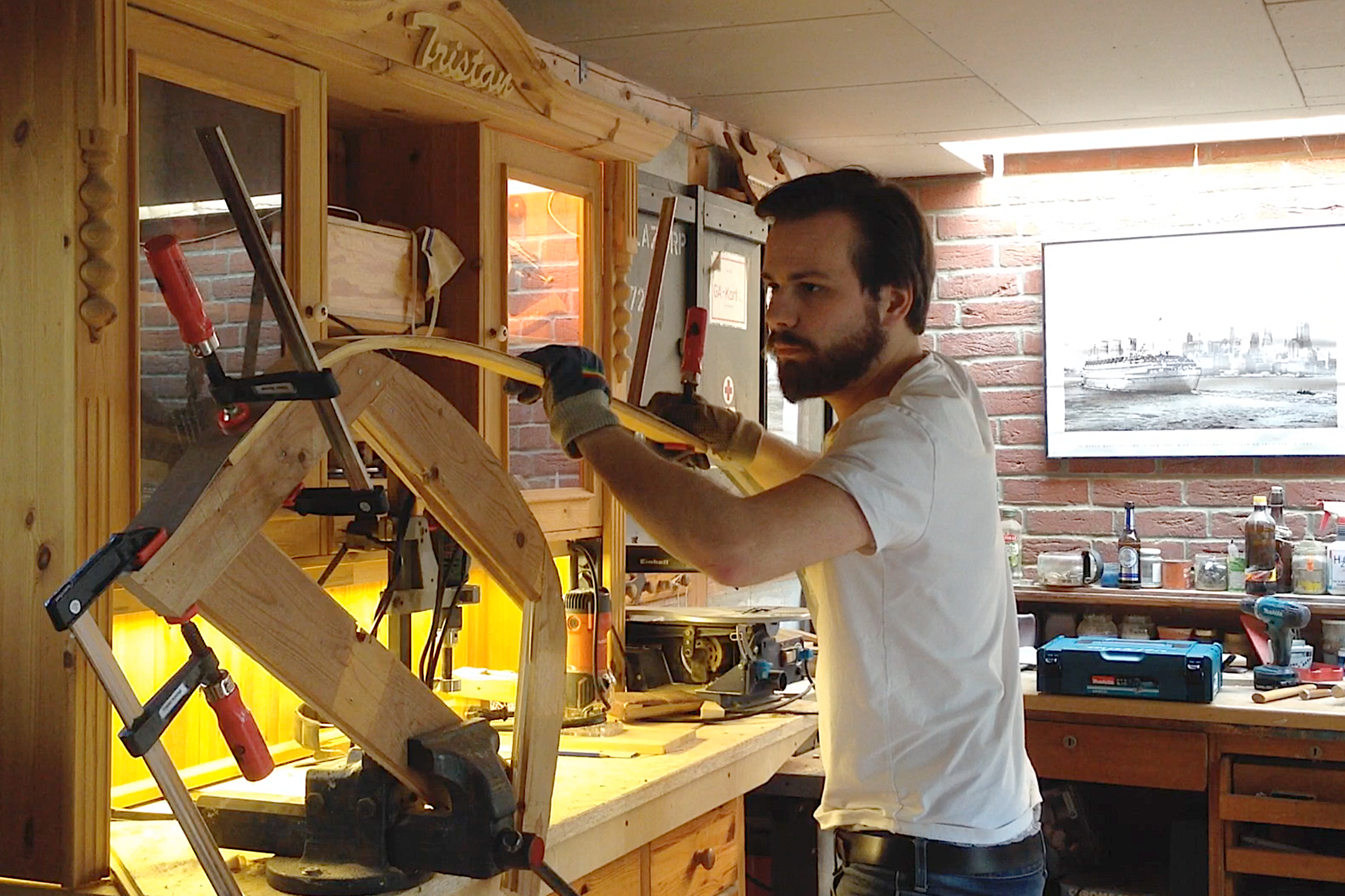 Mann bearbeitet Holz in einer Werkstatt mit Werkzeugen und einer Werkbank.