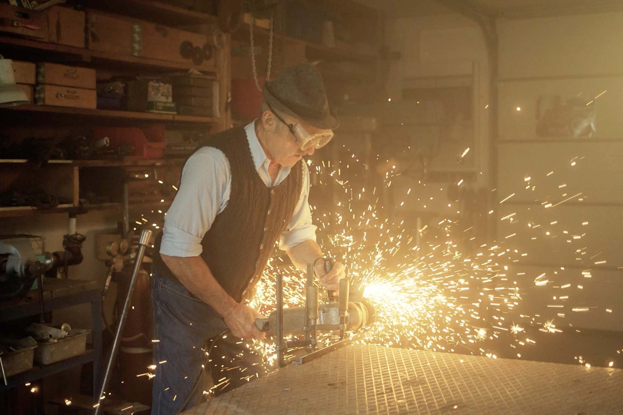 Un homme portant des lunettes de protection travaille le métal avec une meuleuse d'angle, ce qui produit des étincelles.