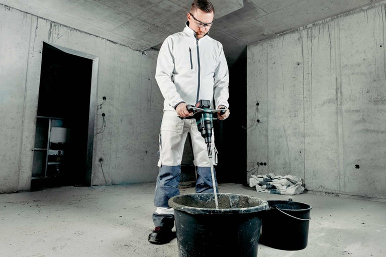 Artisan mélangeant du mortier avec un mélangeur dans un seau sur un chantier de construction.
