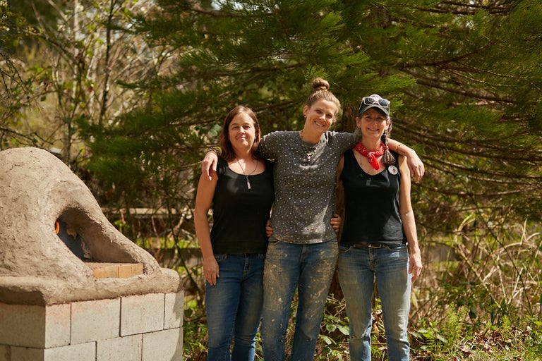 Trois femmes se tiennent devant un four en argile à l'extérieur.