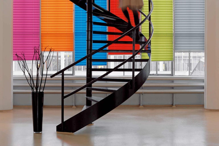 Intérieur avec des stores plissés colorés aux fenêtres et un escalier en colimaçon