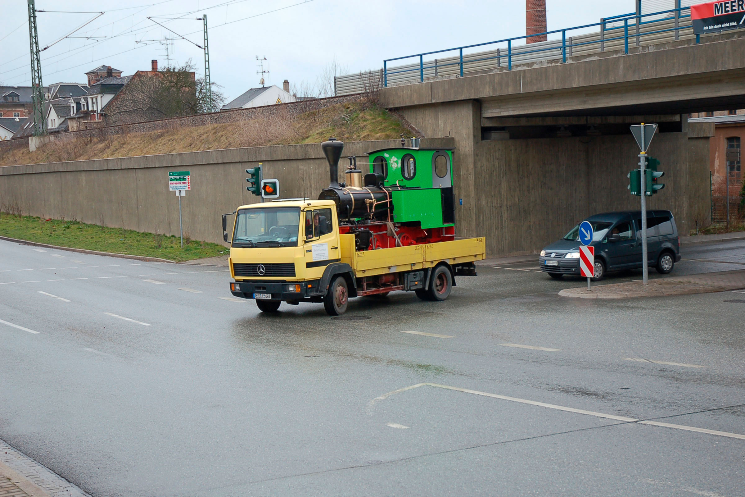 Un camion jaune transporte une locomotive à vapeur miniature verte sur une voie publique.
