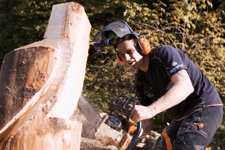Homme coupant du bois avec une tronçonneuse et un équipement de sécurité