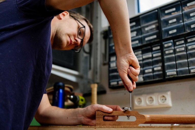 Un homme fixe la mécanique sur une tête de guitare avec un tournevis