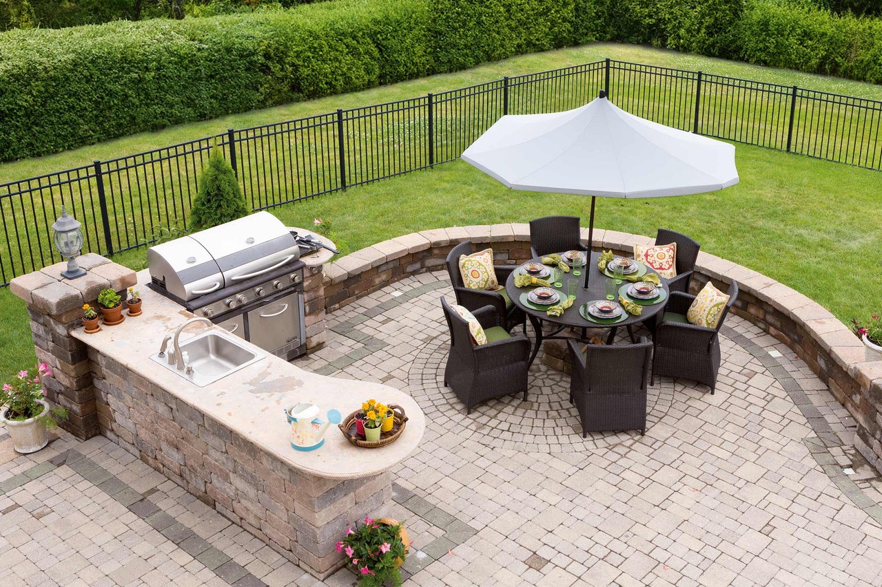 Scène de jardin avec barbecue, évier, table à manger avec parasol et sièges sur une terrasse en pierre