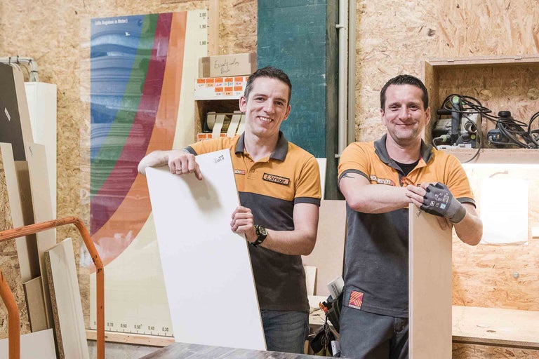 Zwei Mitarbeiter präsentieren eine beschichtete Spanplatte im Hornbach-Baumarkt.