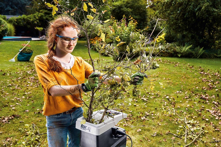 Eine Frau zerkleinert Äste mit einem Gartenschredder von for_q im Garten.