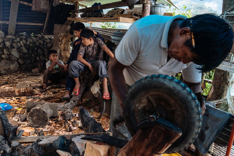 Un homme aiguise un outil avec une meule, tandis que trois enfants regardent