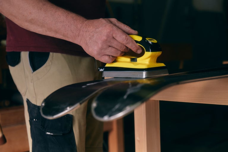 Une personne ponce des skis avec une ponceuse électrique sur un établi.