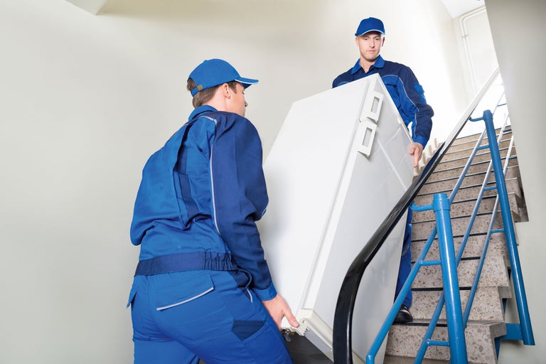 Deux déménageurs montent un réfrigérateur dans l'escalier.