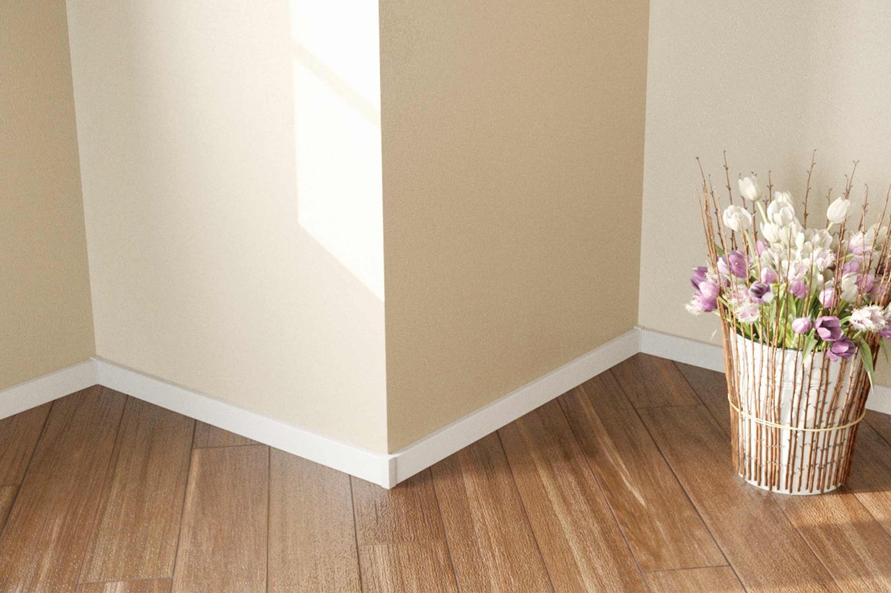 Ecke eines Raumes mit Holzboden, weißen Fußleisten und einem Blumenarrangement