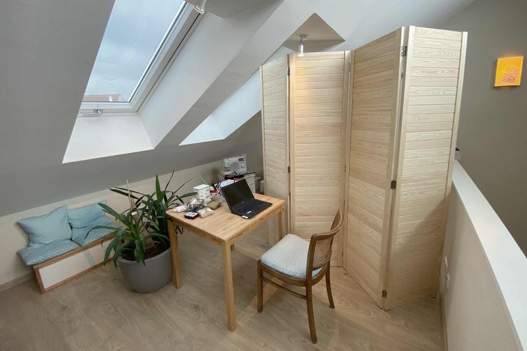 Aménagement d'un bureau mansardé avec bureau en bois, ordinateur portable, plante d'intérieur, chaise en bois et paravent.