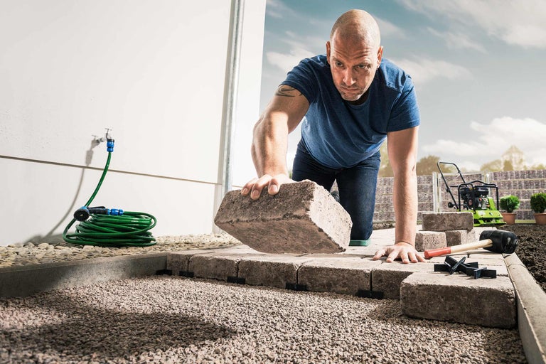 Un homme pose des pavés dans le jardin avec des outils de jardinage
