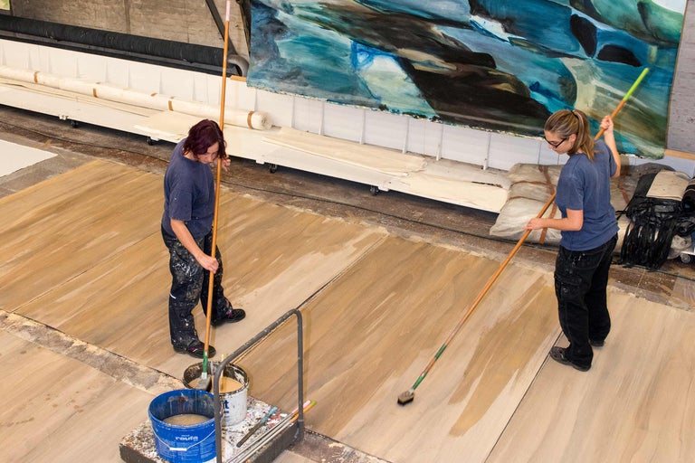 Deux femmes appliquent une lasure de protection du bois sur un plancher en bois avec des pinceaux plats