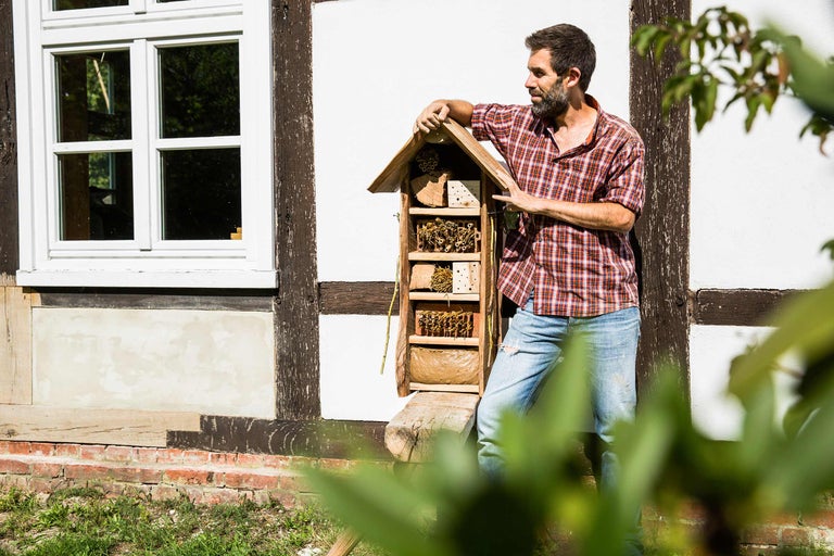 Un homme s'appuie contre un hôtel à insectes dans le jardin devant une maison à colombages.