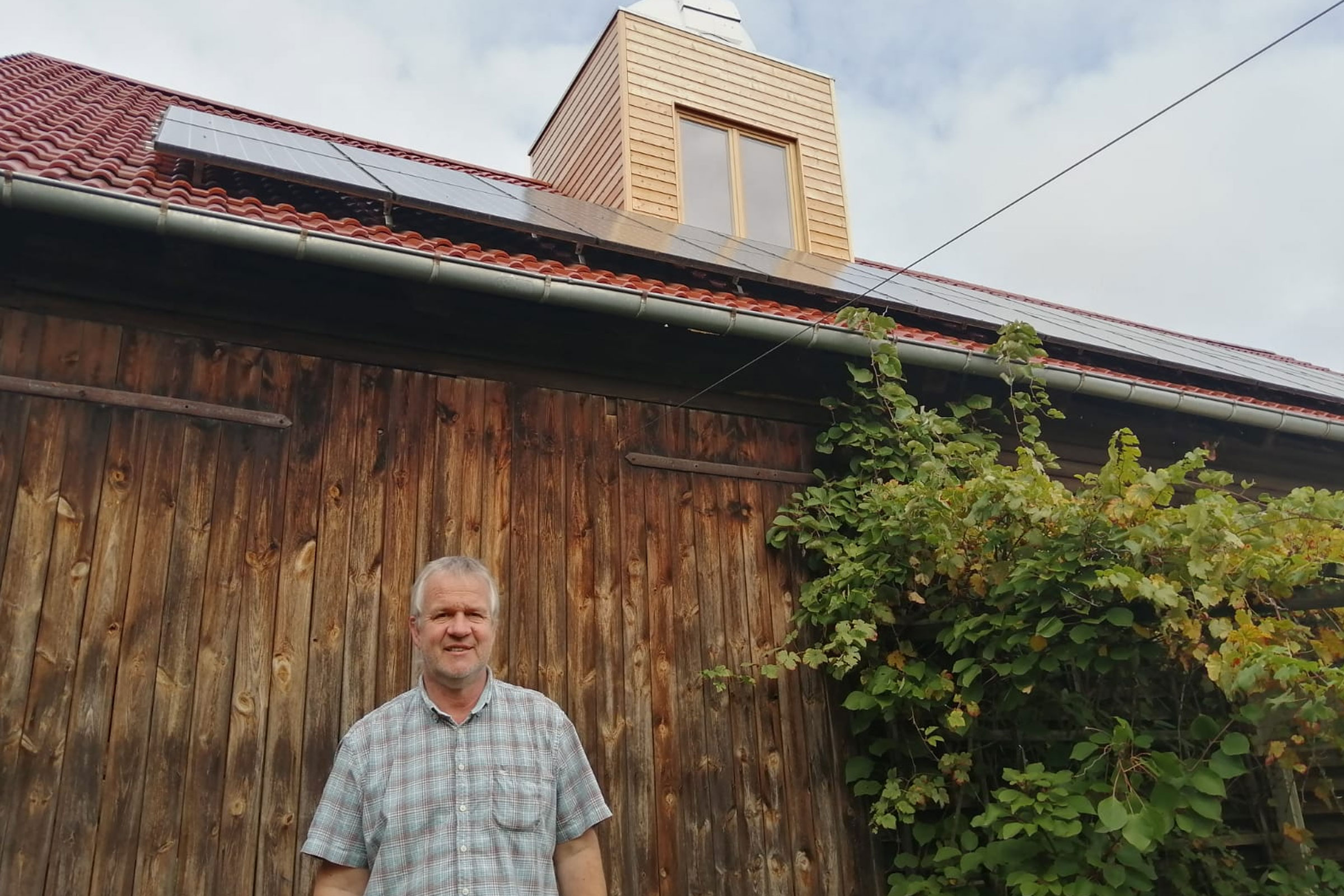 Grange en bois avec des panneaux solaires sur le toit et un homme au premier plan