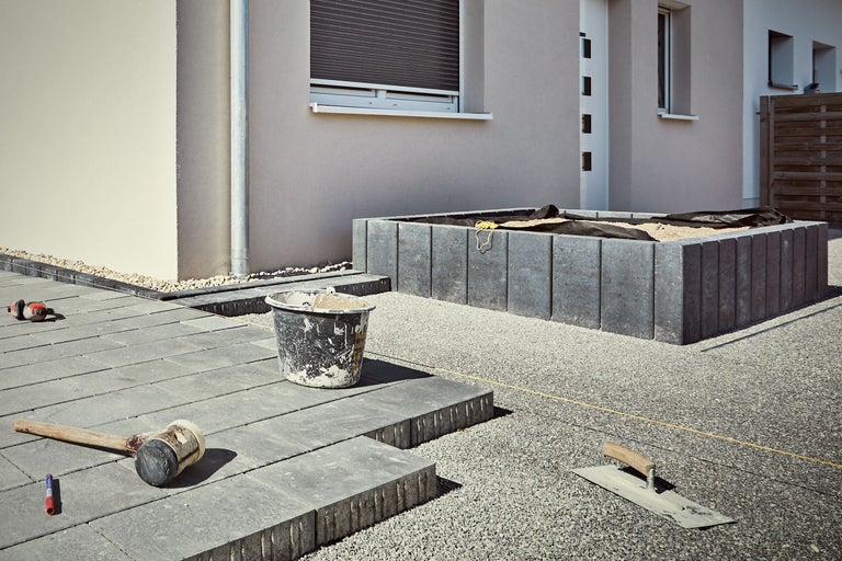 Aussenbereich mit Pflastersteinen, Gummischl Hammer, Maurerkelle und Mörtelkübel vor Hausfassade