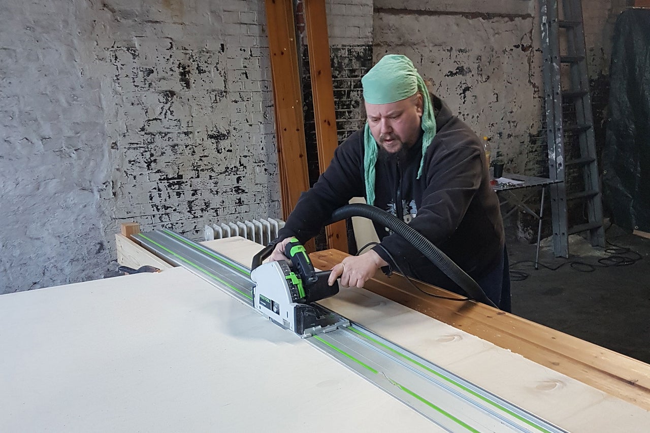 Artisan coupant une plaque avec une scie circulaire portative et un rail de guidage dans un atelier