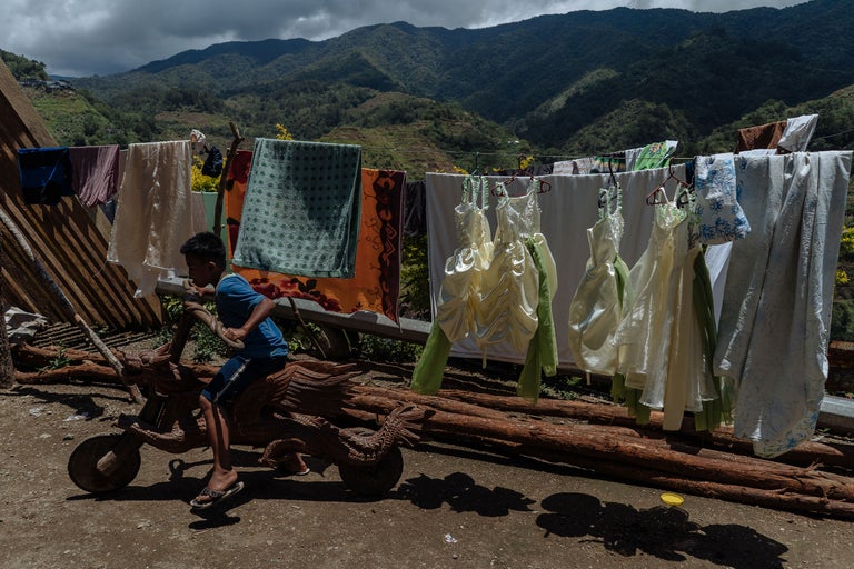 Garçon sur un vélo en bois devant une corde à linge dans un paysage de montagne