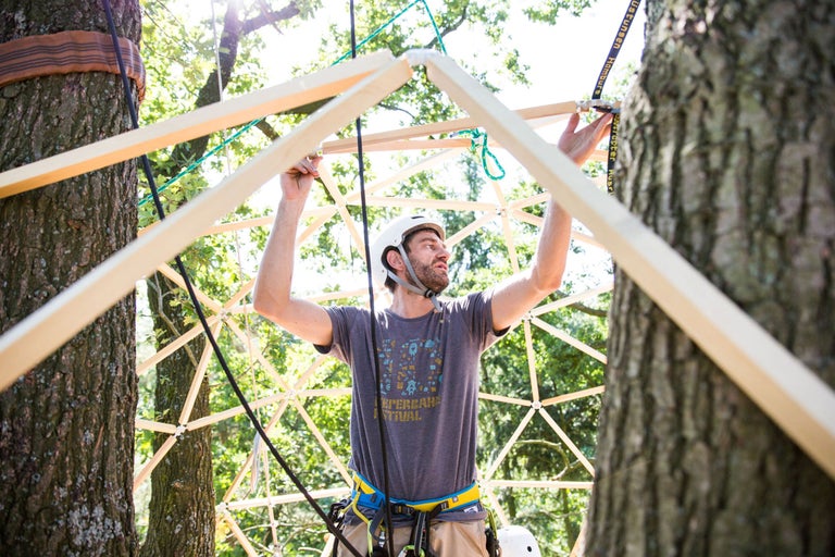 Mann montiert Baumhaus-Rahmen mit Holz und Seilen