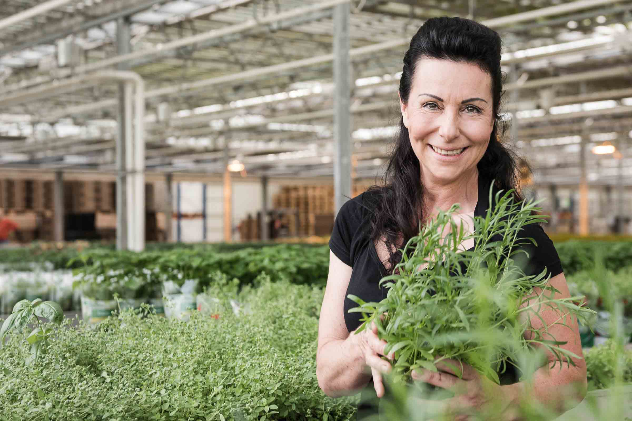 Femme tenant des herbes aromatiques dans une jardinerie.