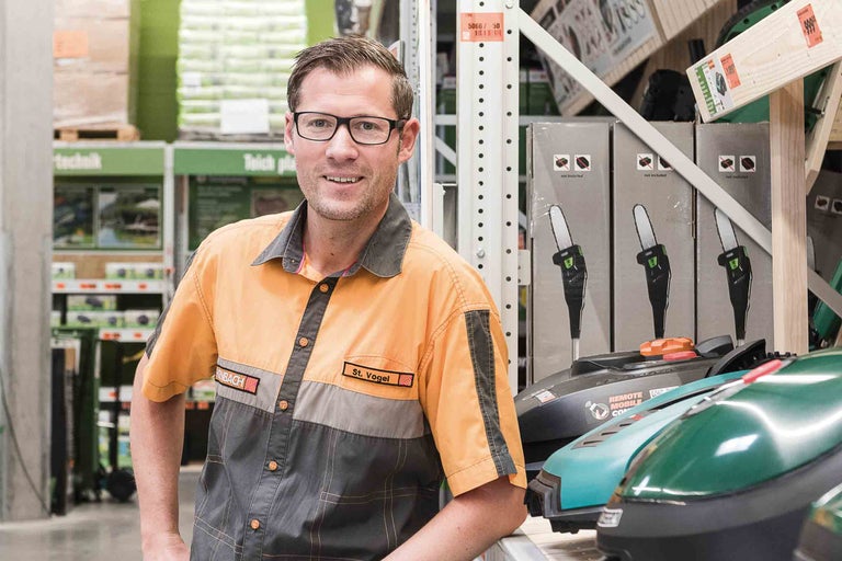 Un employé Hornbach se tient dans le magasin à côté de tondeuses à gazon et de tronçonneuses