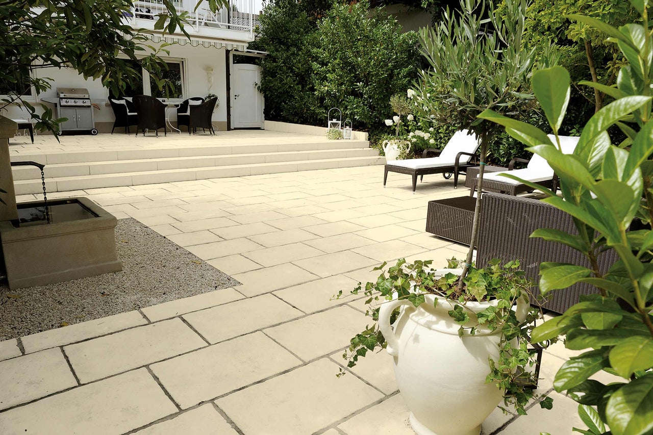 Terrasse avec dalles en pierre, barbecue, meubles de jardin et plantes.