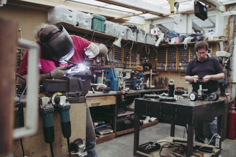 Atelier avec soudeur, établi, outils et étagères.
