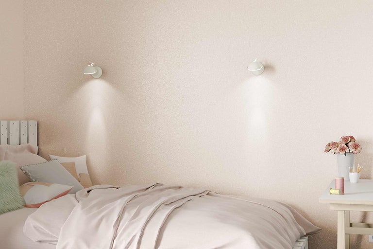 Chambre avec lit, table de chevet et appliques murales devant un papier peint pailleté