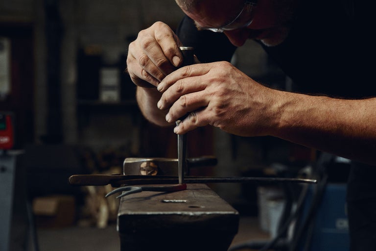 Forgeron travaillant le métal incandescent avec un burin sur une enclume