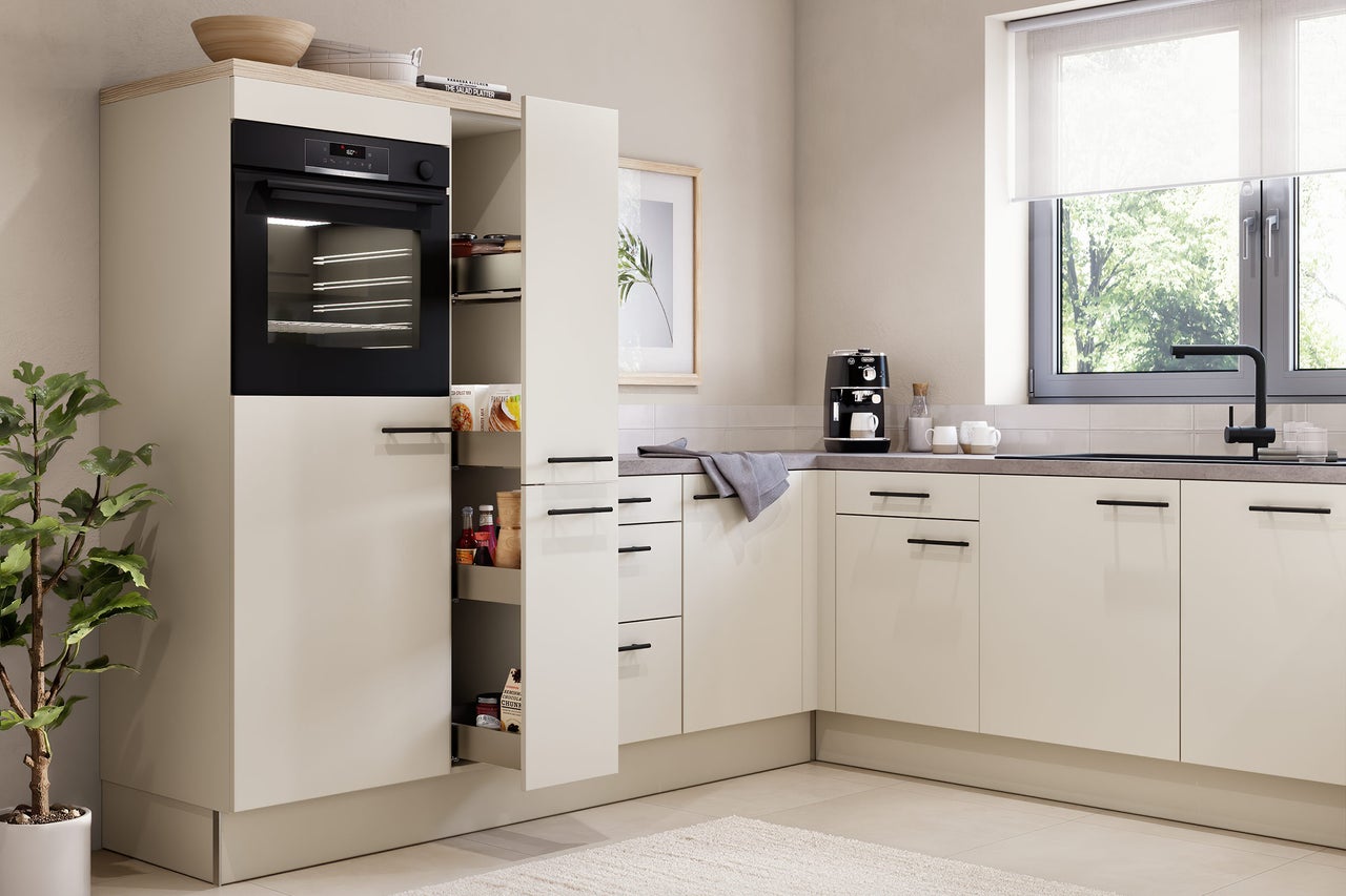 Moderne L-Küche in Beige mit schwarzem Einbaubackofen, Apothekerschrank, grauer Arbeitsplatte und schwarzer Armatur am Fenster.
