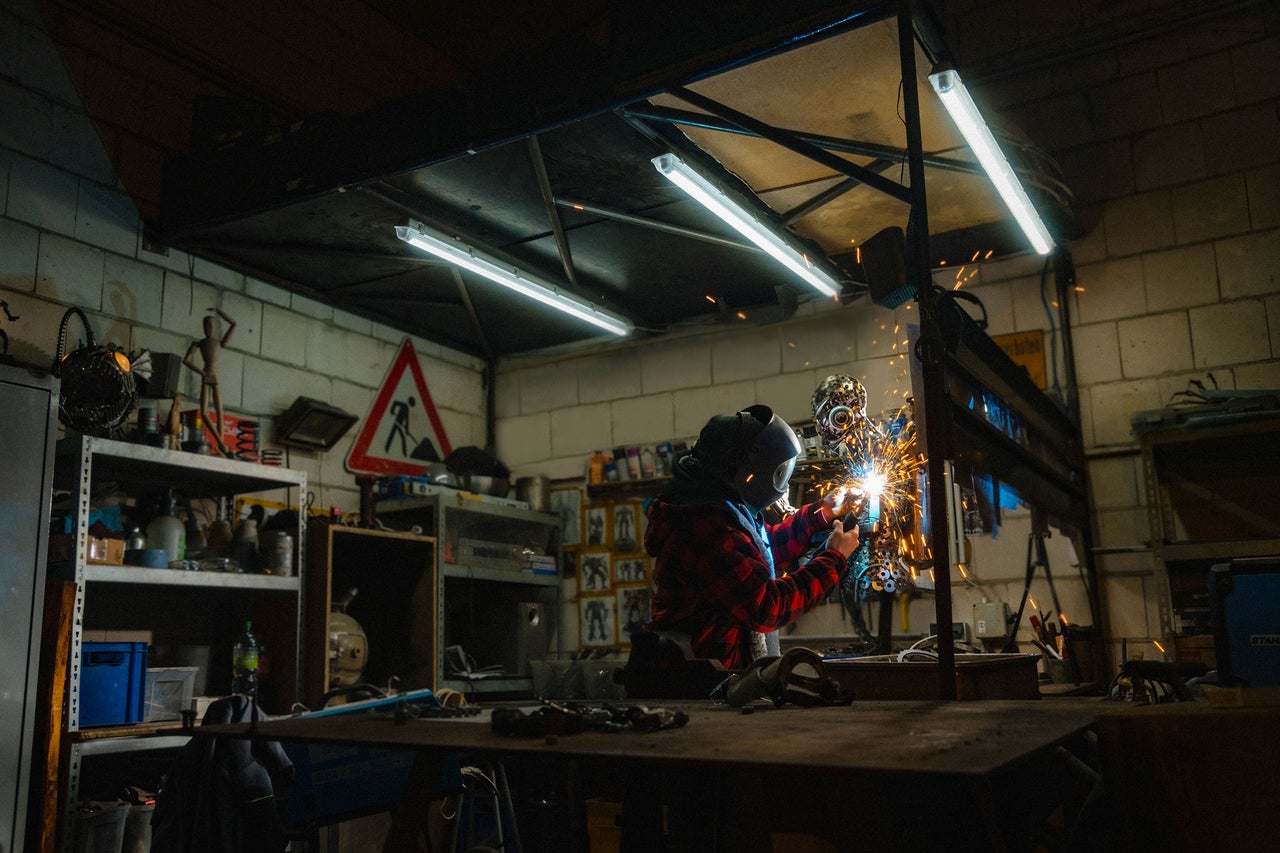 Werkstattansicht mit Schweisser, der mit Schutzkleidung arbeitet und Funken erzeugt.