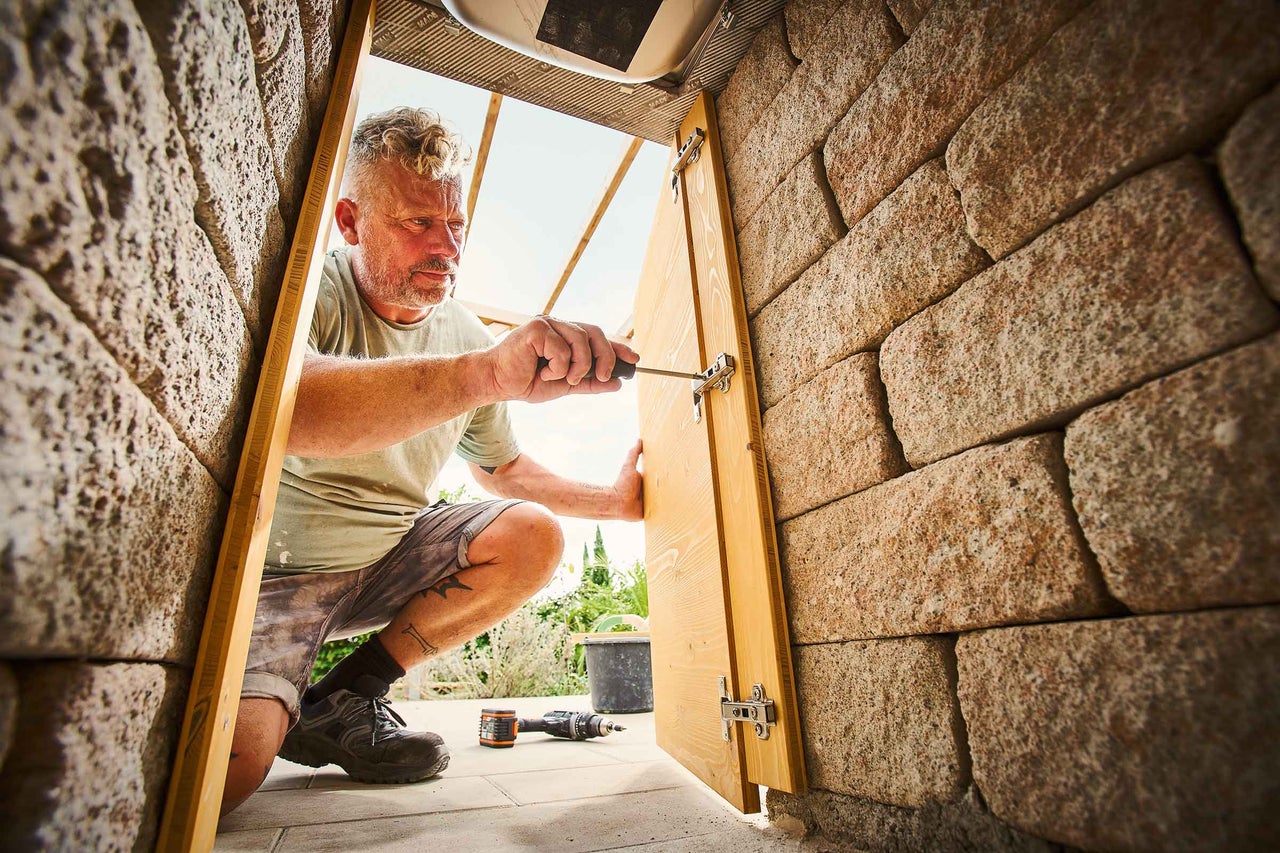 Un homme installe une porte en bois dans un mur avec un tournevis