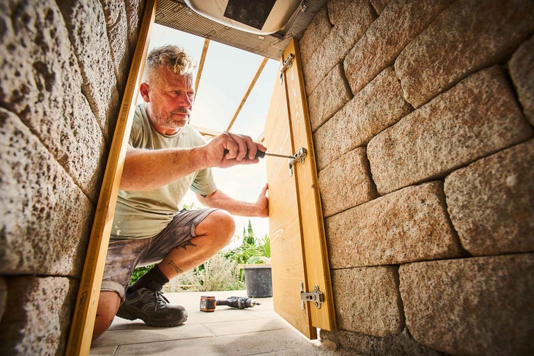 Un homme installe une porte en bois dans un mur avec un tournevis