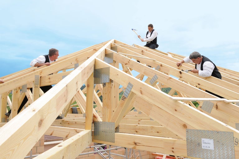 Charpentiers montant un toit à ossature en bois avec des connecteurs métalliques.