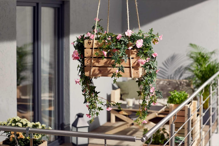 Jardinière suspendue en bois avec fleurs roses et feuilles vertes pour l'extérieur.