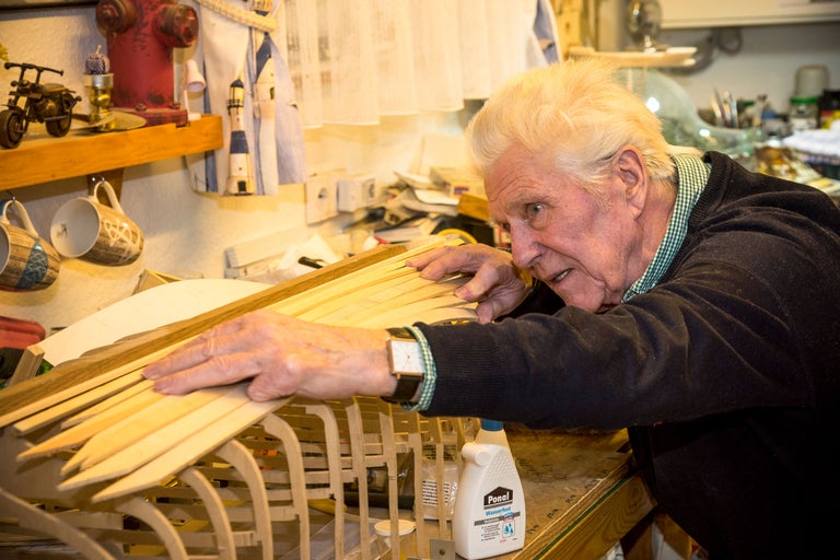 Mann arbeitet an einem Schiffsmodell mit Holzleisten und Klebstoff.