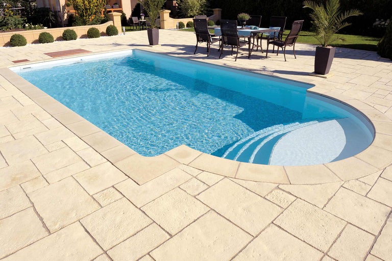 Piscine avec dalles de pierre claires et coin salon dans le jardin