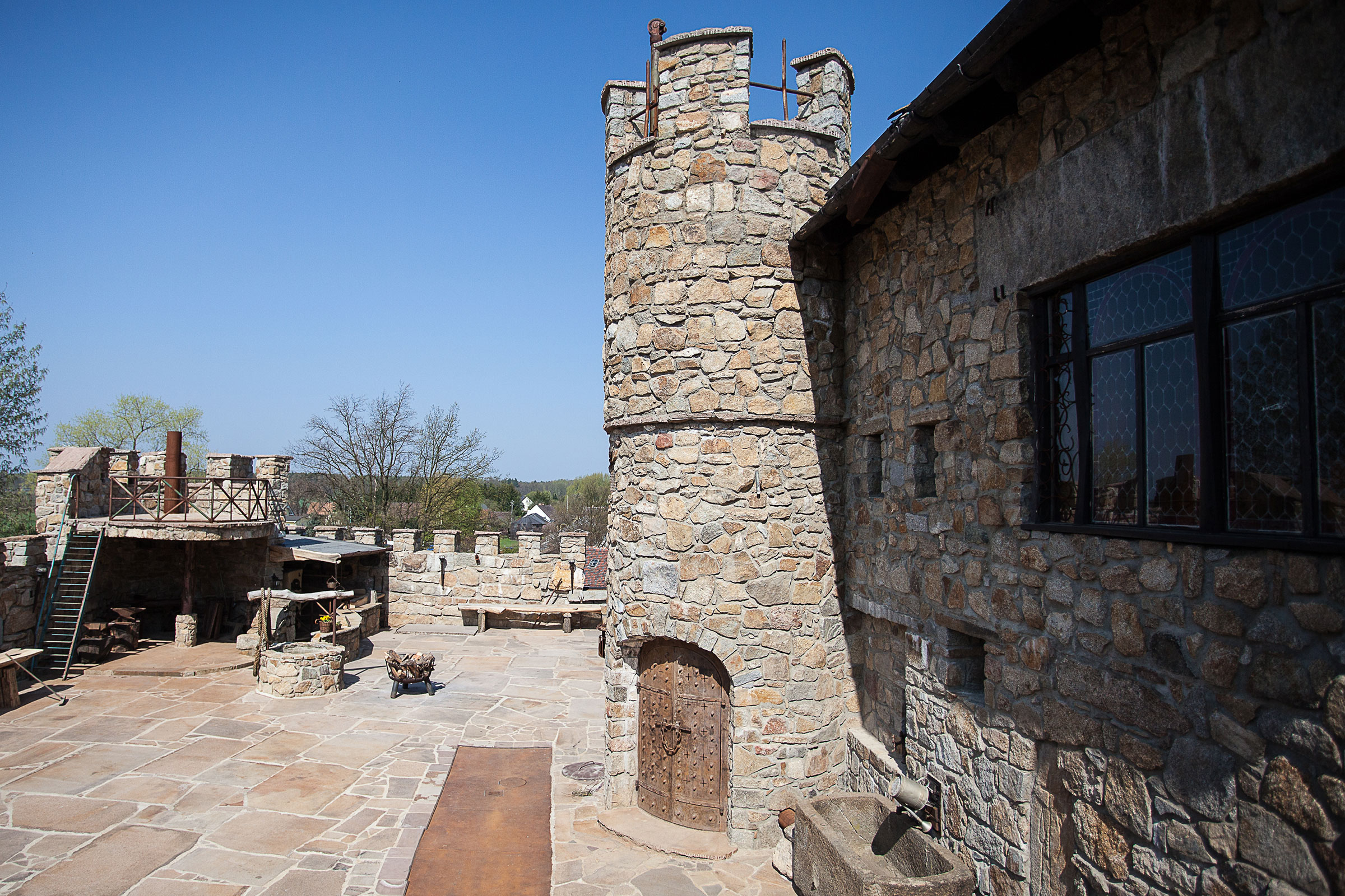 Aussenansicht eines Hauses im Burgstil mit Steinturm und Steinhof