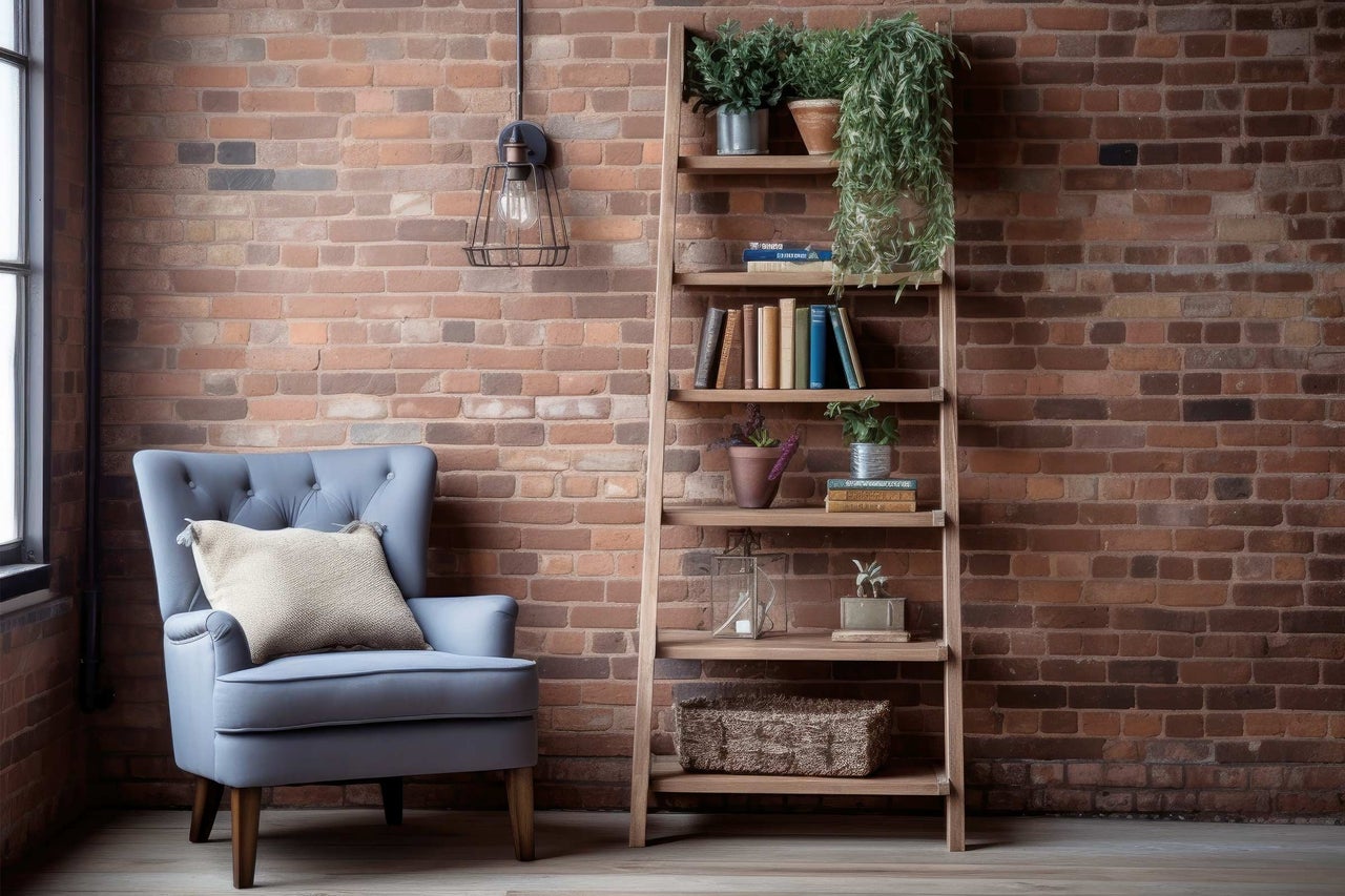 Wohnzimmer mit Sessel, Bücherregal und dekorativen Elementen vor einer Ziegelwand.