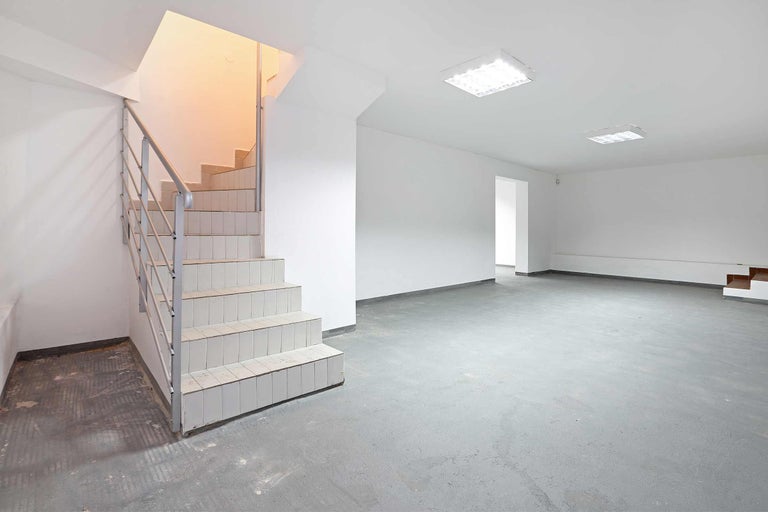 Sous-sol lumineux avec escalier, sol en béton gris et plafonniers